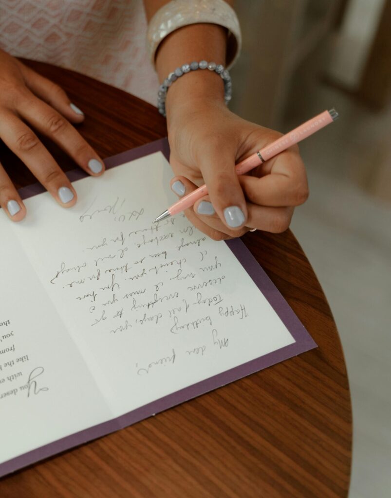 Fotografi av ett par kvinnliga händer. Kvinnan skriver en hälsning i ett gratulationskort.
